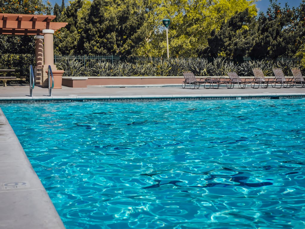 Tranquil poolside scene with sparkling blue water and empty lounge chairs.